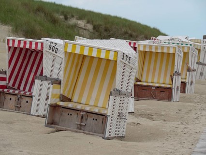 Colourful beach chairs in a row on the sandy beach, surrounded by dunes, pleasant weather without