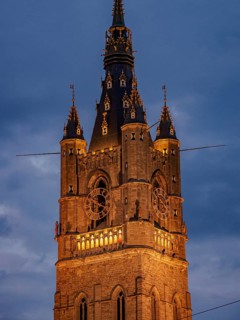 Illuminated clock tower with gothic elements in the evening, blue hour in a medieval town with