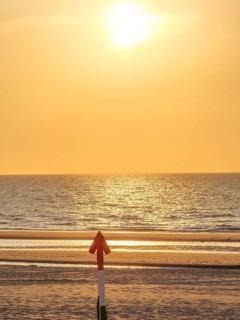 An arrow on the beach points towards the sea at sunset, the sky shines in golden light, sunset on