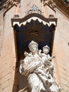 Expressive Madonna statue with child under an elaborate stone canopy on a historic facade, the town