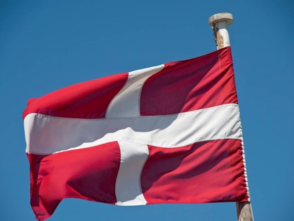 Danish flag flies on a flagpole against a clear sky, the town of mdina on the island of malta with