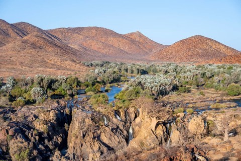 Kunene River with green vegetation in dry red mountain landscape, waterfall and African Baobab