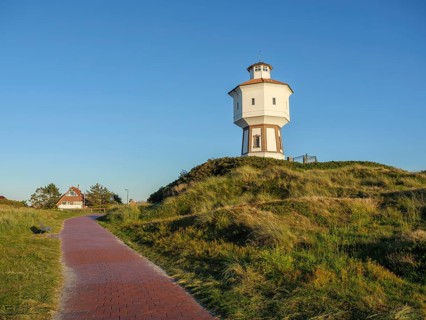 Lighthouse on a hill on a cobbled path with green landscape and houses in the background under a