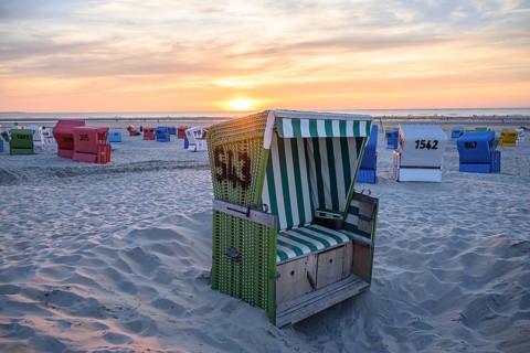 A green beach chair in a pit, surrounded by colourful beach chairs, at sunset, summer evening on