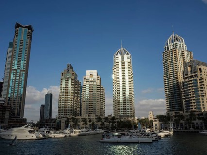 Boats in a marina in front of a row of modern skyscrapers under a cloudless sky, Dubai, Arab