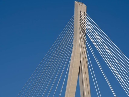 Part of a modern bridge with cable tensions under a clear blue sky, the old town of Dubrovnik with