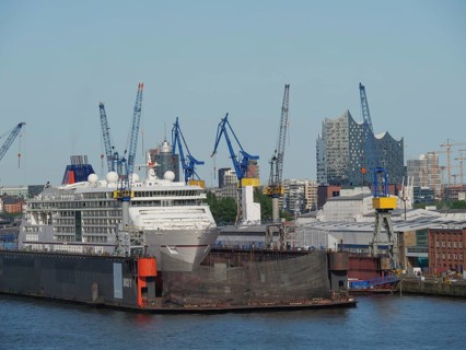 A large ship in the harbour of Hamburg with cranes and the Elbe Philharmonic Hall concert hall in