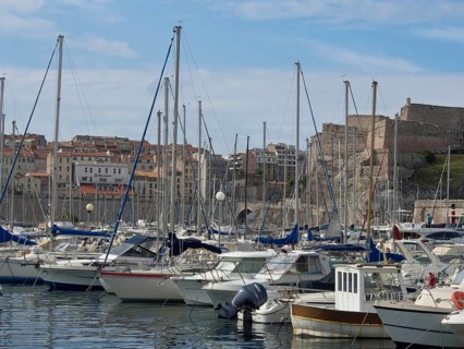 A marina full of boats with buildings and a hill behind it, Marseille on the Mediterranean Sea with