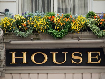 A richly decorated windowsill with colourful flowers above a sign with the inscription 'House',