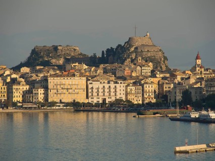 Historic town with a large fortress on a hill, surrounded by numerous buildings and a quiet harbour