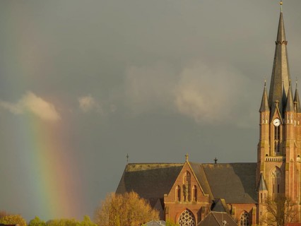 A gothic church with a high tower under a cloudy sky and a rainbow in the background, rainbow at a