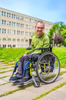 Man in wheelchair smiling at camera outside the university in the campus with green grass