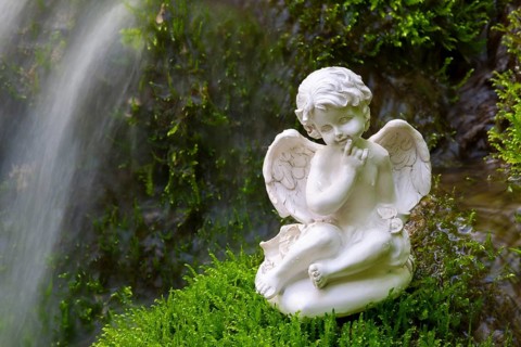 Porcelain angel figurine on moss by a waterfall