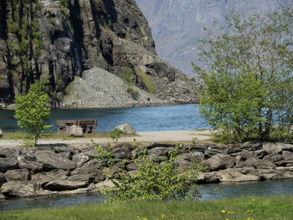 Cosy lake with mountains in the background, trees and a bench on the shore, spring in the fjord