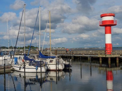 Harbour view with sailing boats, jetty and a red and white lighthouse, calm water and clouds in the