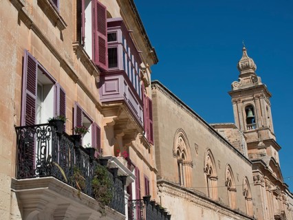Row of historic buildings with balconies and shutters under a clear sky, the town of mdina on the