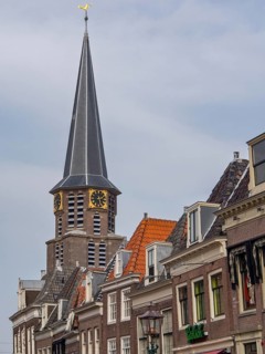 Church tower with clock and surrounding historic buildings under a blue sky, historic houses in