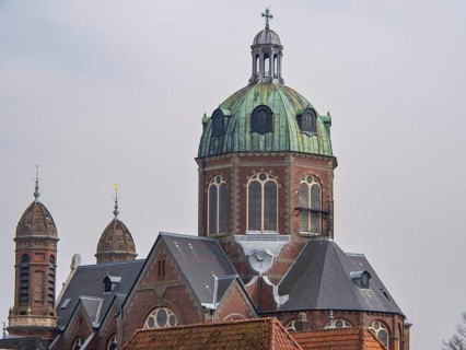 A church building with a central green dome and two smaller towers, under a cloudy sky, historic