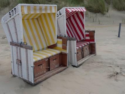 Two beach chairs, one yellow and one red, on the sandy beach in front of the dunes, the north sea