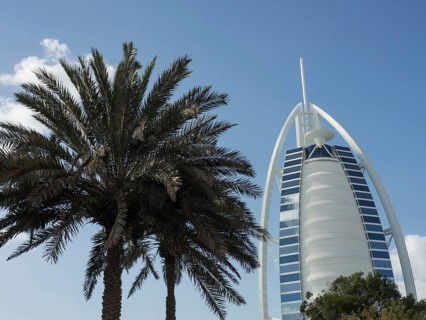 Burj Al Arab, a modern landmark, in front of a blue sky with a palm tree in the foreground, Dubai,