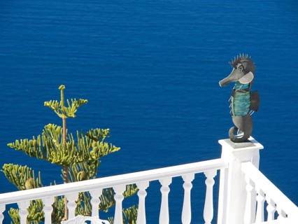 Seahorse sculpture on a railing in front of a deep blue sea and blue sky in Greece, The volcanic