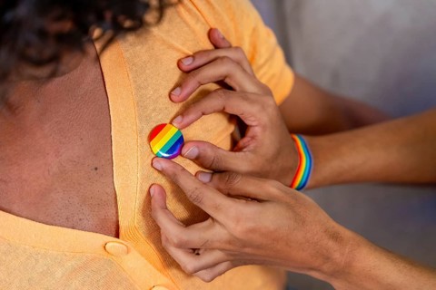 Close-up of gay man pinning a LGBT badge on his couple sitting on the sofa