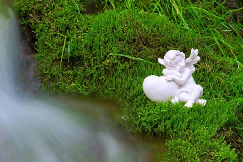 Porcelain angel figurine on moss by a waterfall