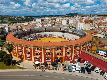 Bullring with red and yellow accents in the middle of a city under a cloudy sky, with parked cars