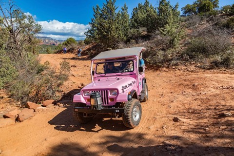 Pink jeep from Pink Jeep Tours passes hikers resting along the rough road used by off-road vehicles