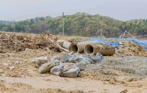 Old dirty concrete culvert sections on ground beside tree branches at construction site in Daejeon,