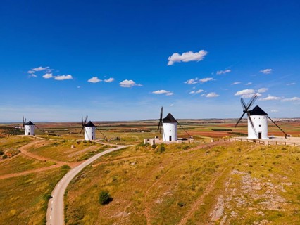 Four windmills stand on a hill under a bright blue sky in a vast summer landscape, aerial view,