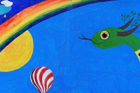 Colourful mural with a snake, sun, rainbow and a hot air balloon under a clear sky, mural, East