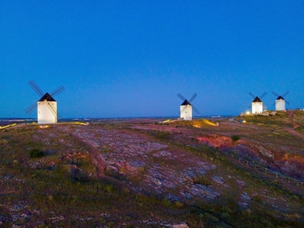 Several windmills on a hill at dusk in a wide field landscape under a clear sky, aerial view,