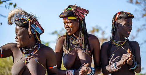 Hakaona woman with traditional kapapo hairstyle, clapping and laughing, Angolan tribe of the