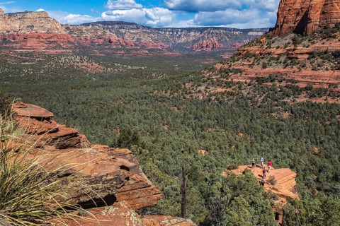 Hikers climb to the top of a red rock sandstone formation along the Devil's Bridge Trail in Sedona,