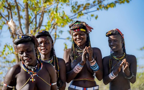 Hakaona woman with traditional kapapo hairstyle, clapping and laughing, Angolan tribe of the