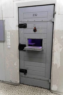 Close-up of a grey prison door with food window and security devices, Berlin-Hohenschoenhausen