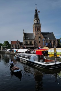 A cargo of cheese being transported down a canal next to a cheese market taking place in front of