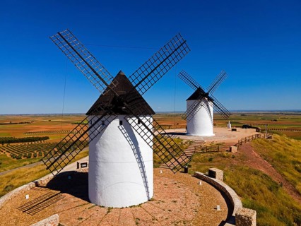Two windmills stand on a sunny hill in a wide field landscape under a clear sky, aerial view,
