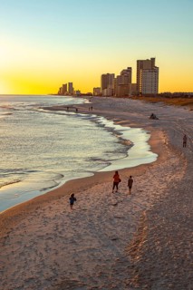 People walking and playing on the beach as the sun sets over the Gulf of Mexico at Gulf Shores,