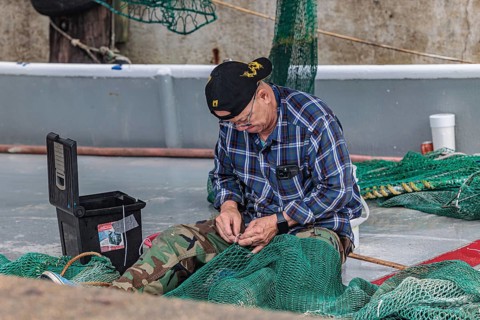 Commercial fisherman on his shrimp boat repairing his nets at the Biloxi Small Craft Harbor in