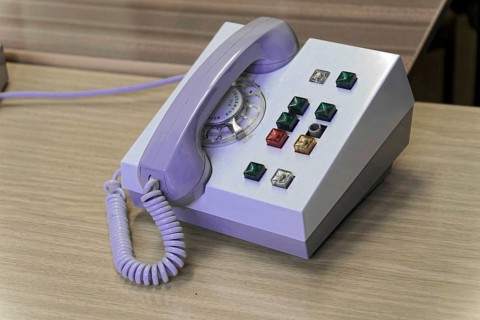Close-up of an old rotary-disc telephone with various control buttons on a wooden desk,