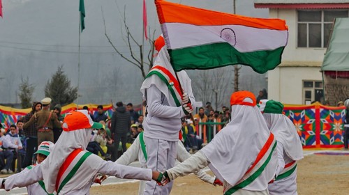 Children in white uniforms holding the Indian flag while participating in a parade filled with