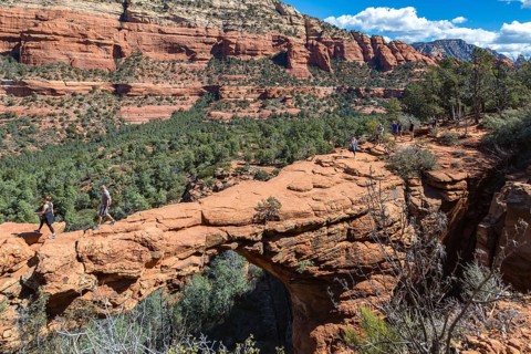 Hikers cross the Devil's Bridge natural arch along the Devil's Bridge Trail in Sedona, Arizona,
