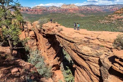 Hikers cross the Devil's Bridge natural arch along the Devil's Bridge Trail in Sedona, Arizona,
