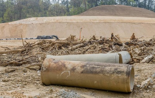 Old dirty concrete culvert sections on ground in front of tree branches at construction site in