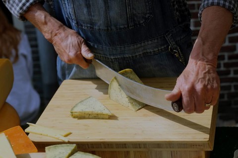 A man in traditional clothing cuts cheese into slices for tasting at the Alkmaar cheese market.,