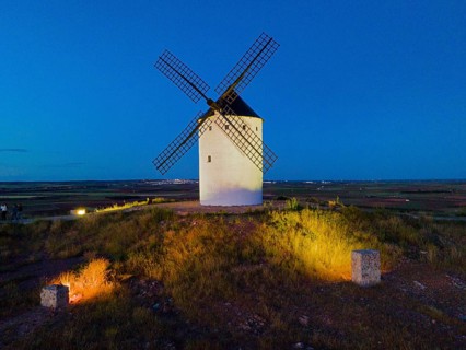 An illuminated windmill on a field hill at dusk under a clear blue sky, aerial view, Alcazar de San