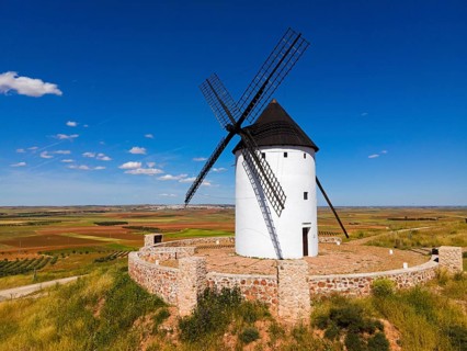 A single windmill on a hill under a bright blue sky in a vast summer landscape, aerial view,