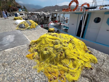 Yellow fishing net lying on quay in front of fishing boat in small harbour of Agia Galini, Agia